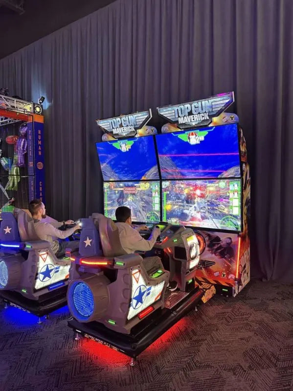 Two people playing a video game in a themed arcade setup with colorful screens and seats.